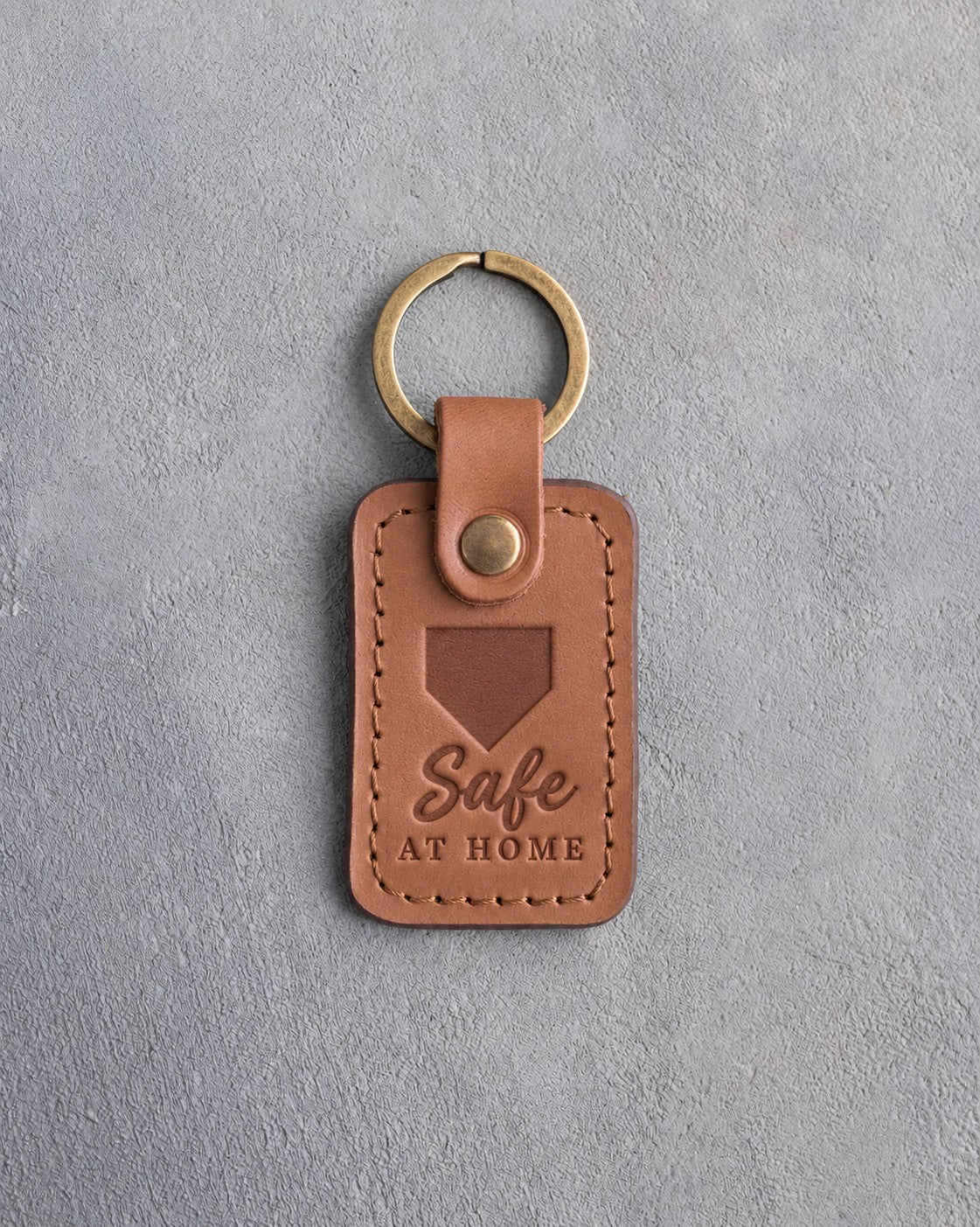 Caramel leather keychain debossed with a home plate and the words Safe AT HOME, on gray plaster