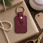 Wine red Safe at Home for Christmas keychain on kraft wrapping paper beside a fir sprig and a new baseball