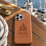 Caramel Molly FAIR WINDS iPhone case in full-grain leather on the worn teak cockpit table of a sailboat beside a coiled white dock line