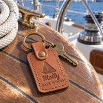 Caramel Molly FAIR WINDS keychain in full-grain leather on the worn teak cockpit table of a sailboat beside a coiled white dock line
