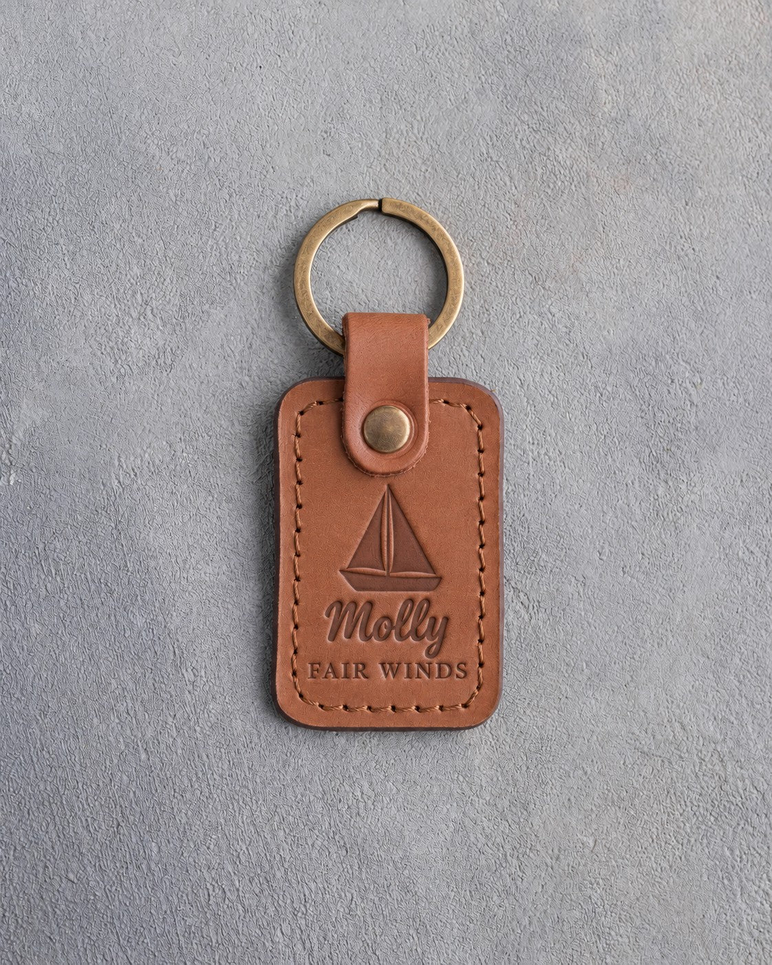 Caramel leather keychain debossed with a sloop under full sail above Molly and FAIR WINDS, on gray plaster