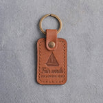 Caramel leather keychain debossed with a sloop under full sail above Fair winds and FOLLOWING SEAS, on gray concrete