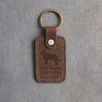 Sicilian brown leather keychain debossed with a Saint Bernard above Saint Bernard and THE SAINT, on gray concrete