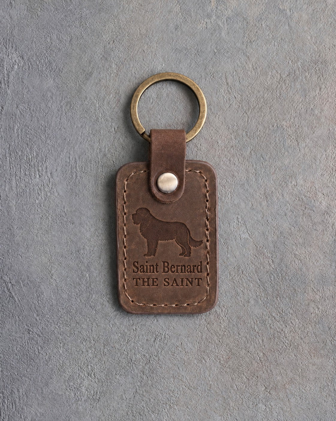 Sicilian brown leather keychain debossed with a Saint Bernard above Saint Bernard and THE SAINT, on gray concrete