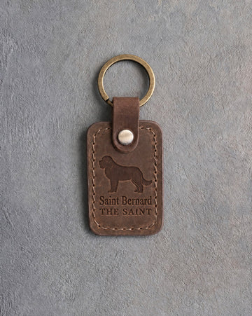 Sicilian brown leather keychain debossed with a Saint Bernard above Saint Bernard and THE SAINT, on gray concrete