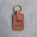 Caramel leather keychain debossed with a steer silhouette above Sale barn and REGULAR, on gray plaster