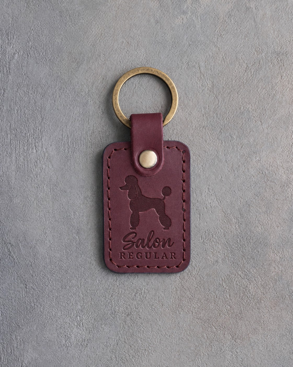 Sangria red leather keychain debossed with a Poodle silhouette and the words Salon REGULAR, on gray concrete