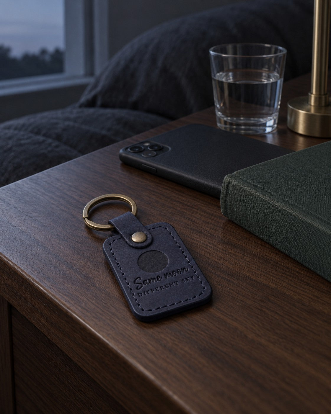 Two navy Same Moon Different Sky keychains on separate key rings beside a handwritten letter at night