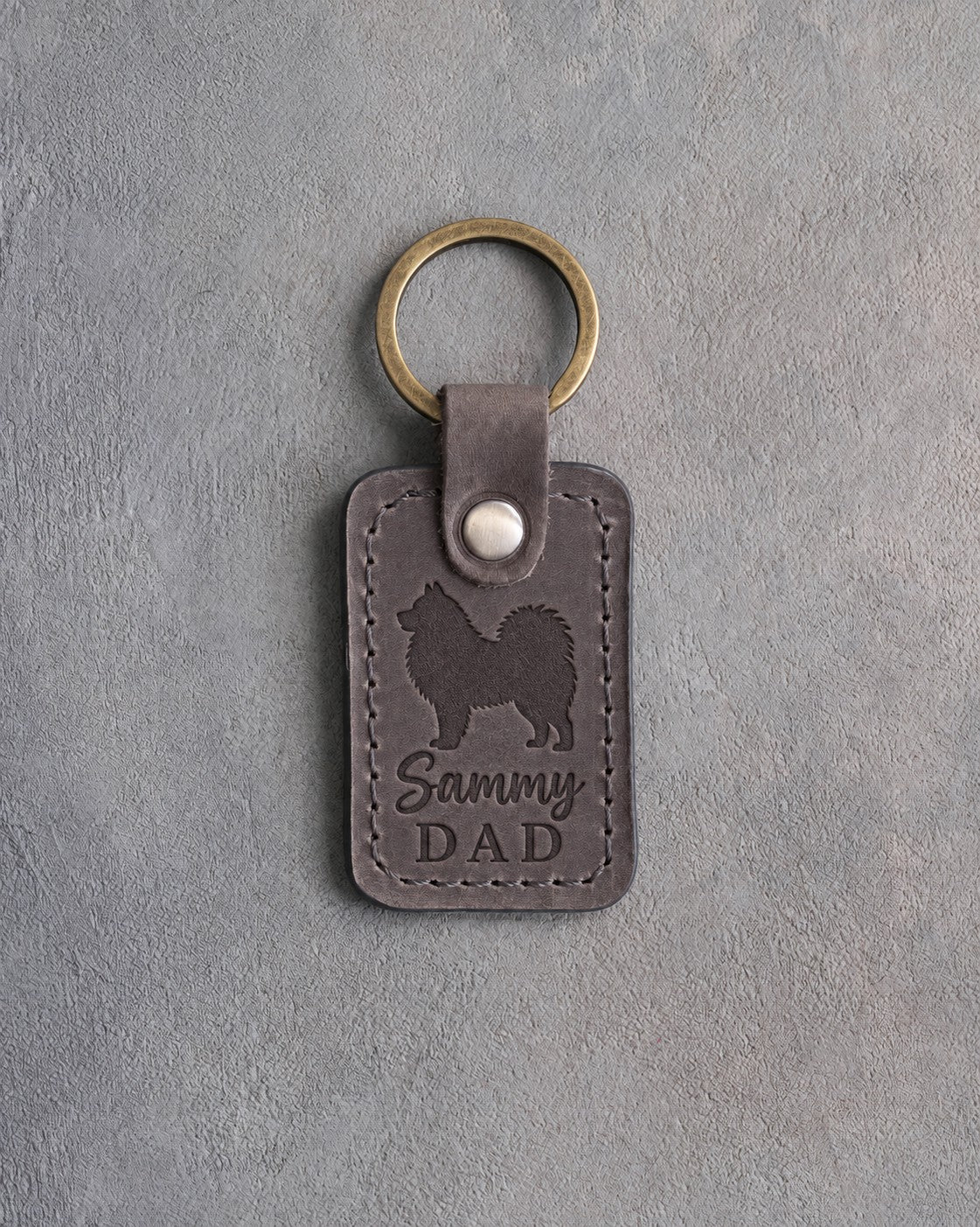 Country gray leather keychain debossed with a Samoyed silhouette and Sammy DAD, on gray concrete