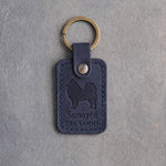 Blueberry navy leather keychain debossed with a Samoyed above Samoyed and THE SAMMY, on gray concrete
