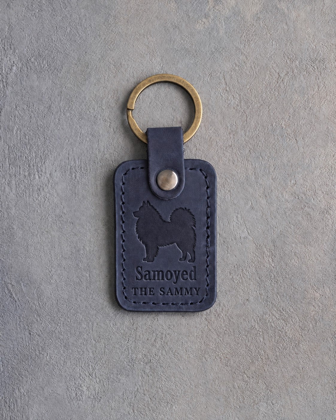Blueberry navy leather keychain debossed with a Samoyed above Samoyed and THE SAMMY, on gray concrete