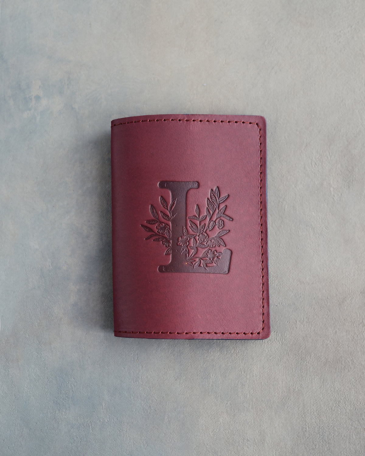 Sangria leather passport cover with a large floral initial L pressed into the front