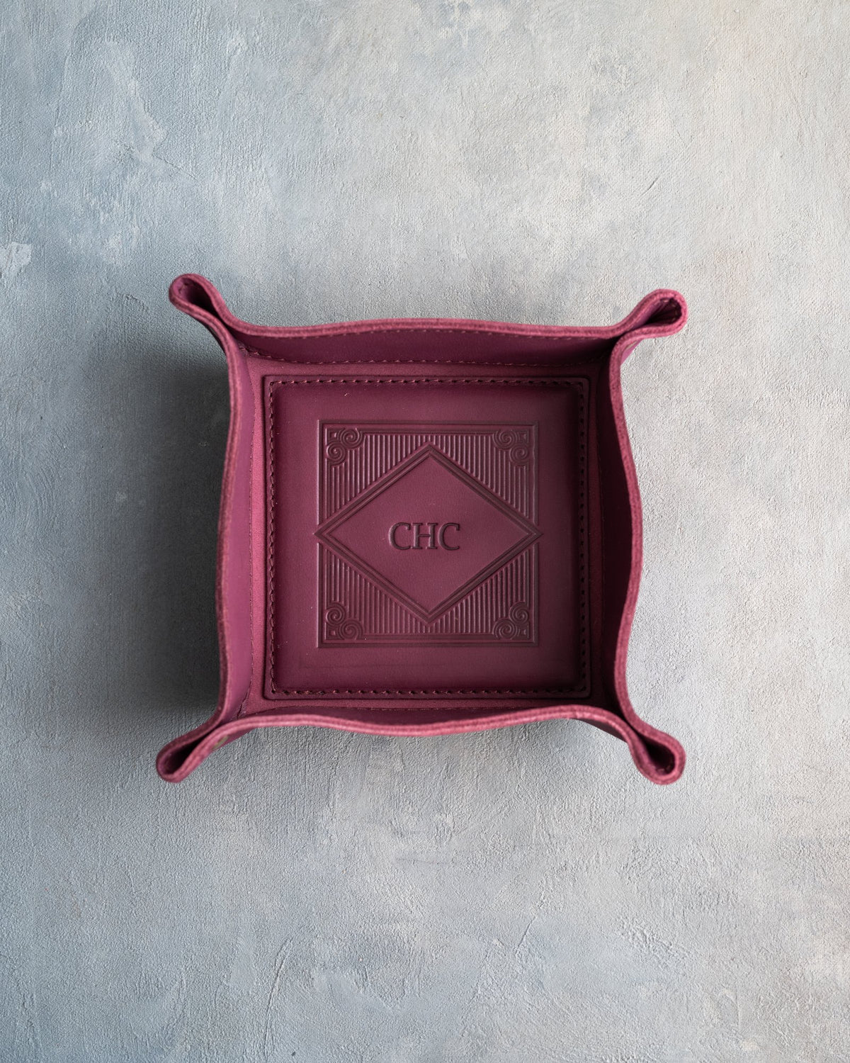 Sangria leather valet tray with snapped corners and the initials CHC pressed into the diamond frame, seen from above