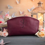 Sangria burgundy leather makeup bag with a floral monogram deboss, roses and a lit lantern in the background