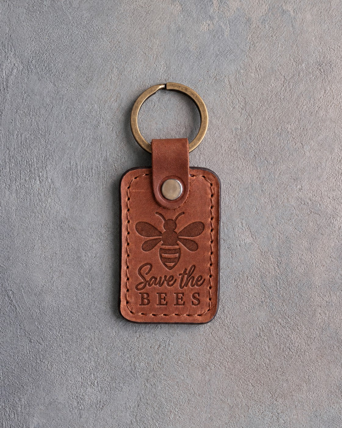 Arizona tan leather keychain debossed with a honeybee above Save the BEES, on gray concrete