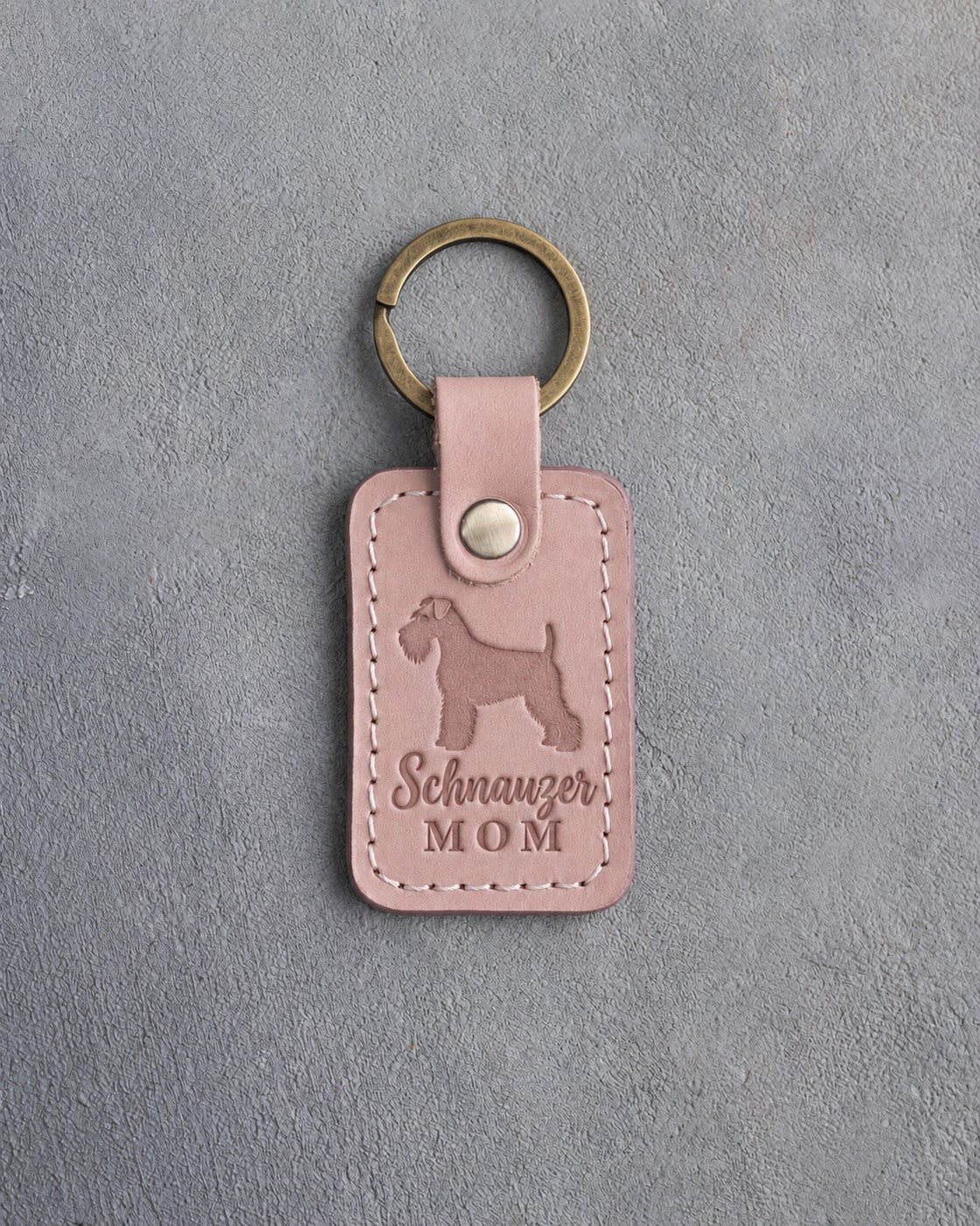 Blush pink leather keychain debossed with a Miniature Schnauzer silhouette and the words Schnauzer MOM, on gray concrete