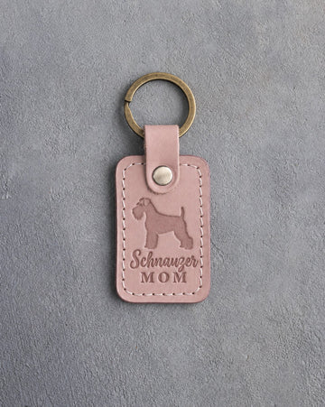Blush pink leather keychain debossed with a Miniature Schnauzer silhouette and the words Schnauzer MOM, on gray concrete