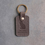 Country gray leather keychain debossed with a Scottish Fold sitting upright above Life with a and SCOTTISH FOLD, on gray concrete