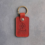 Poppy red leather keychain debossed with a compass rose and the words Search AND RESCUE, on gray concrete