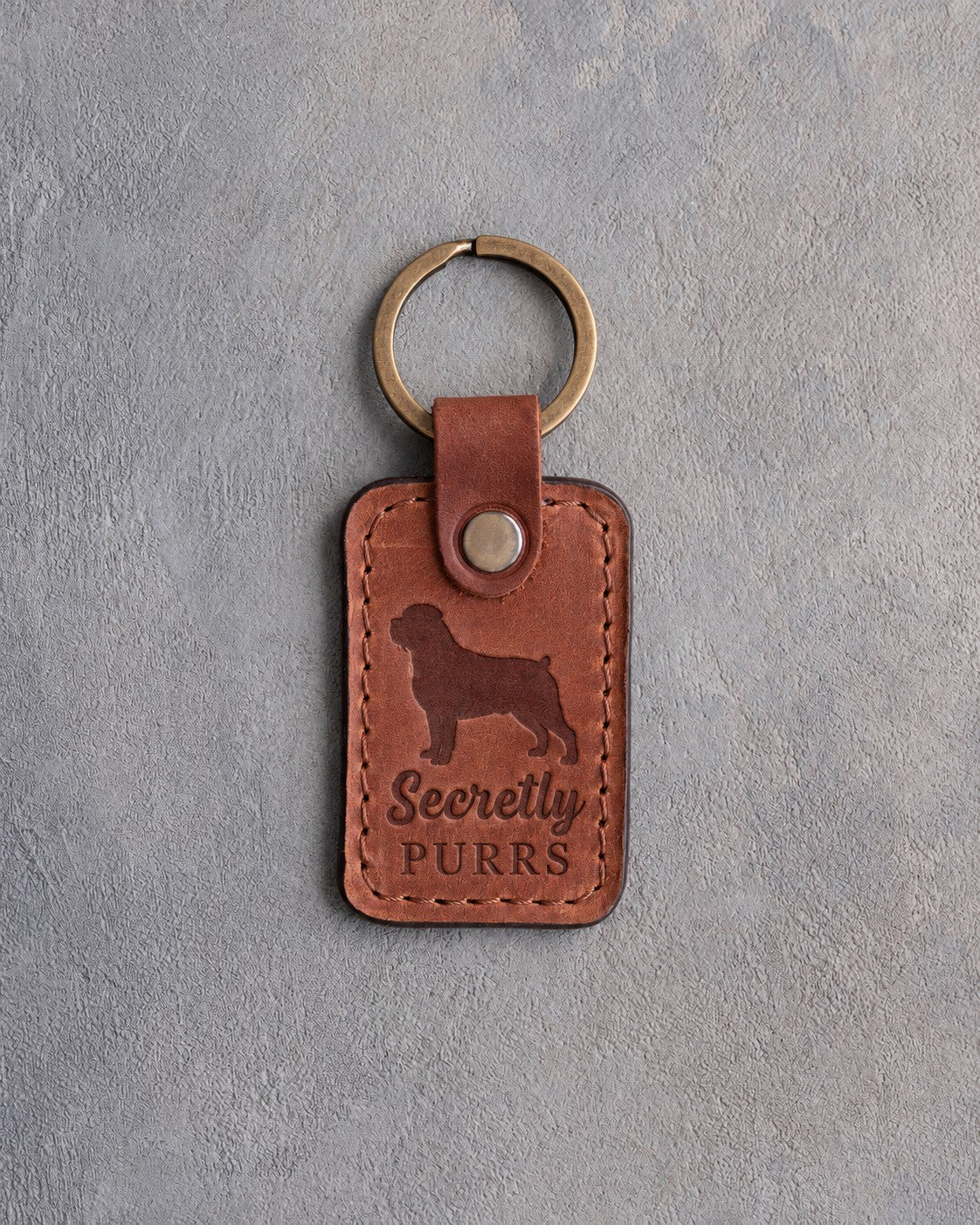 Arizona tan leather keychain debossed with a Rottweiler silhouette and the words Secretly PURRS, on gray concrete