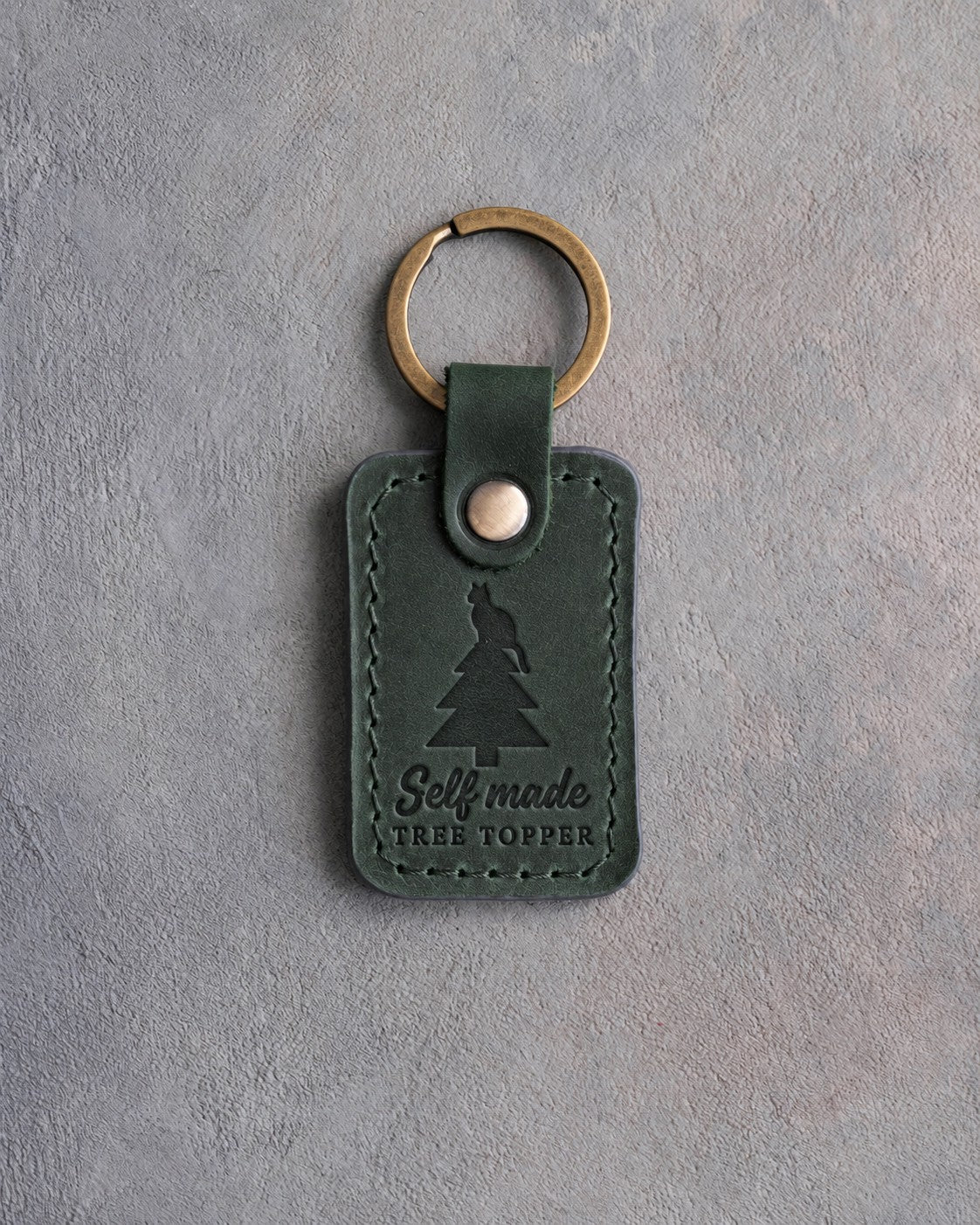 Forest green leather keychain debossed with a cat sitting on top of a Christmas tree above the words Self made TREE TOPPER