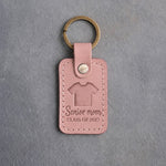 Blush pink leather keychain debossed with a sports jersey above the words Senior mom and CLASS OF 2027, on gray concrete
