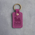 Fuchsia pink leather keychain debossed with a Lhasa Apso silhouette and the words Sentinel OF THE SOFA, on gray concrete