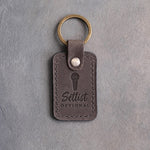Country gray leather keychain debossed with a handheld microphone above the words Setlist OPTIONAL, on gray plaster