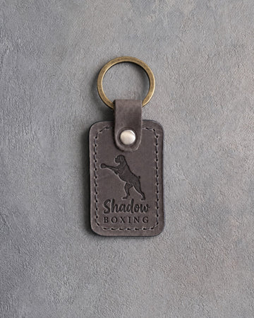 Country gray leather keychain debossed with a boxer on its hind legs throwing a jab and the words Shadow BOXING, on gray concrete