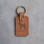 Caramel leather keychain debossed with a Shar Pei silhouette above THE SHAR PEI, on gray concrete