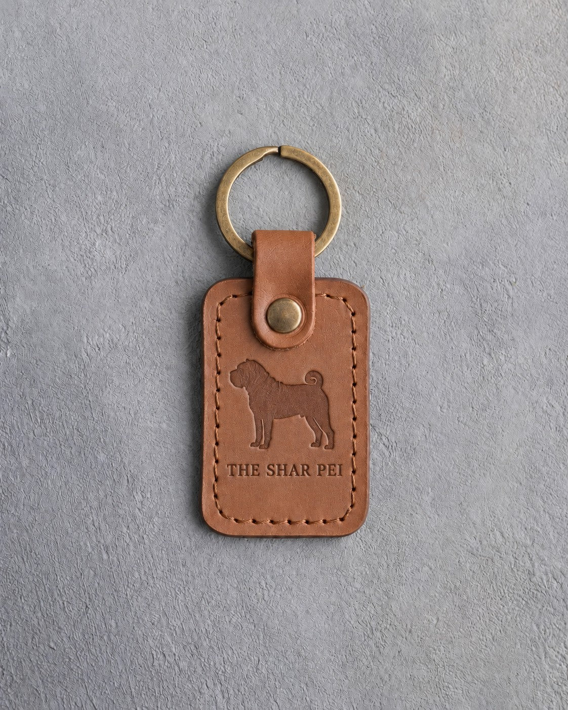 Caramel leather keychain debossed with a Shar Pei silhouette above THE SHAR PEI, on gray concrete