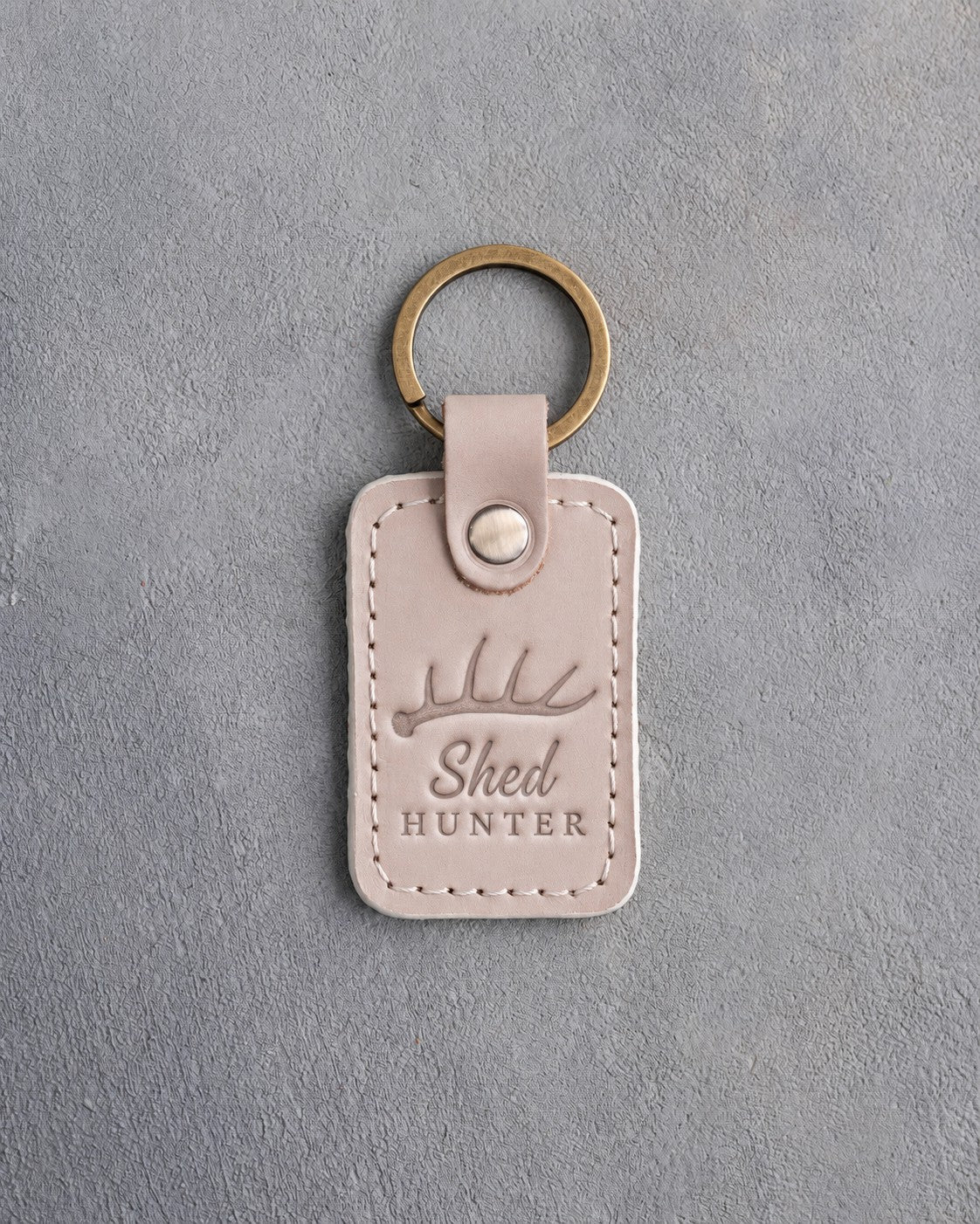 Gray sand leather keychain debossed with a single shed antler above the words Shed HUNTER, on gray plaster