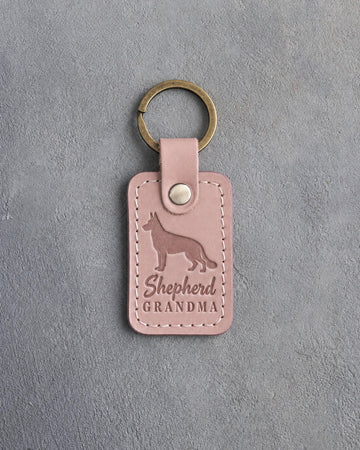 Blush pink leather keychain debossed with a German shepherd silhouette and the words Shepherd GRANDMA, on gray concrete