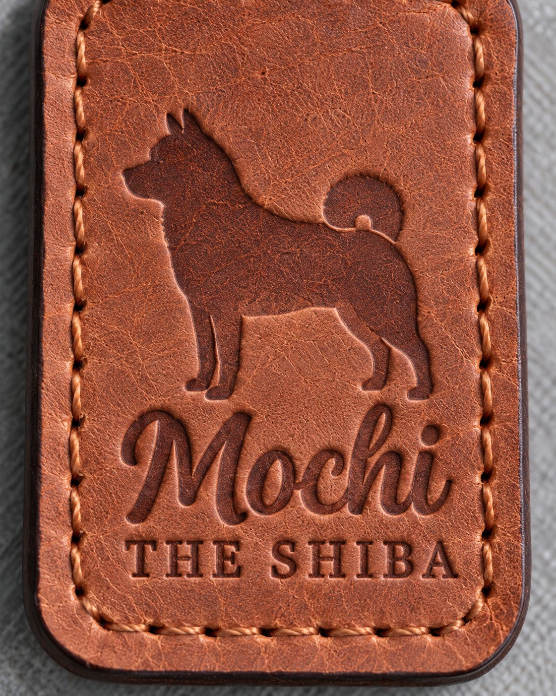 Close-up of Mochi in brush script and THE SHIBA pressed into Arizona tan full-grain leather beneath a Shiba Inu silhouette