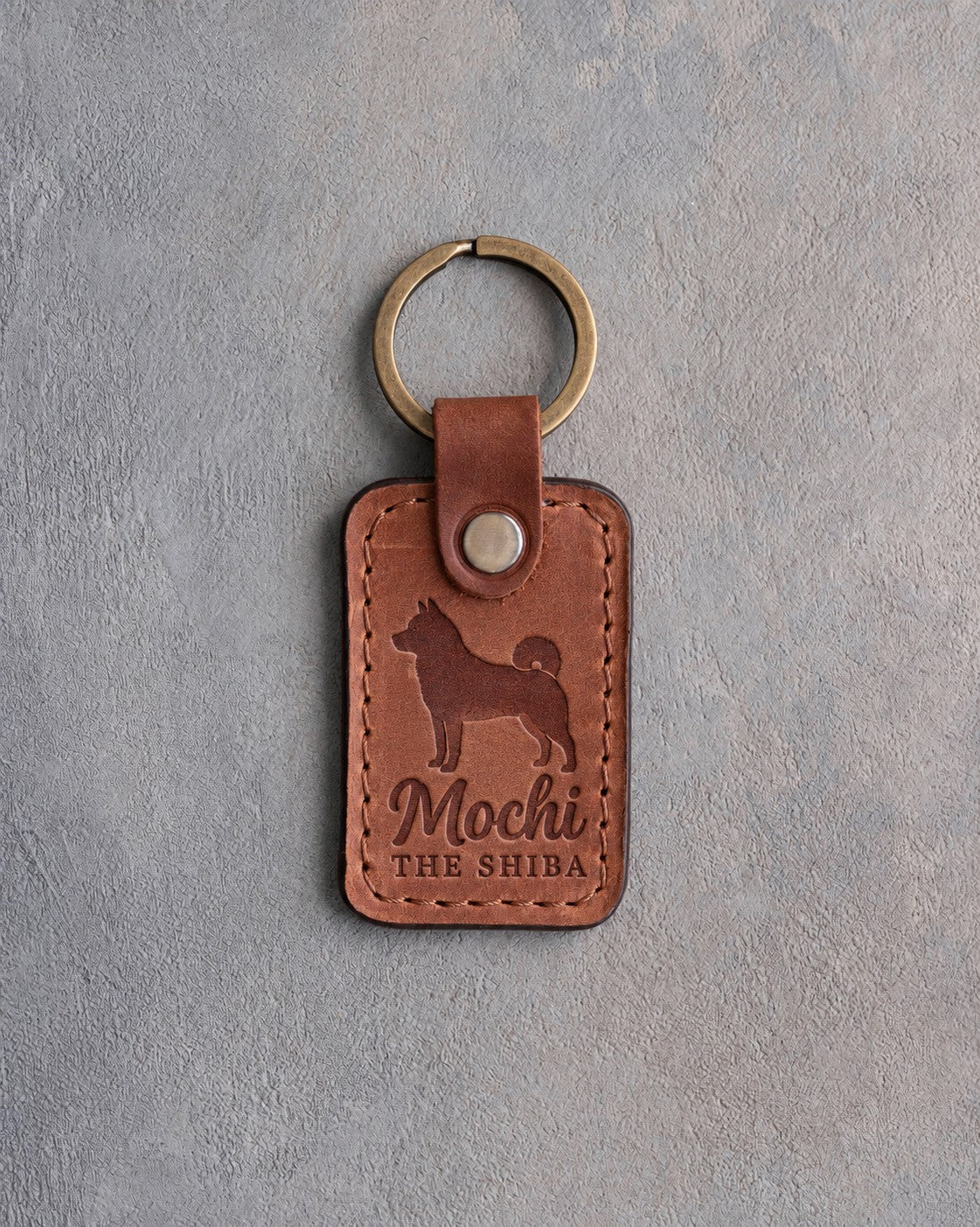 Arizona tan leather keychain debossed with a Shiba Inu silhouette, the name Mochi and THE SHIBA, on gray concrete