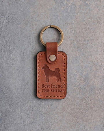 Arizona tan leather keychain debossed with a Shiba Inu silhouette above Best friend and THE SHIBA, on gray concrete