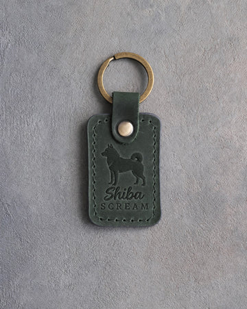 Forest green leather keychain debossed with a Shiba Inu silhouette and the words Shiba SCREAM, on gray concrete