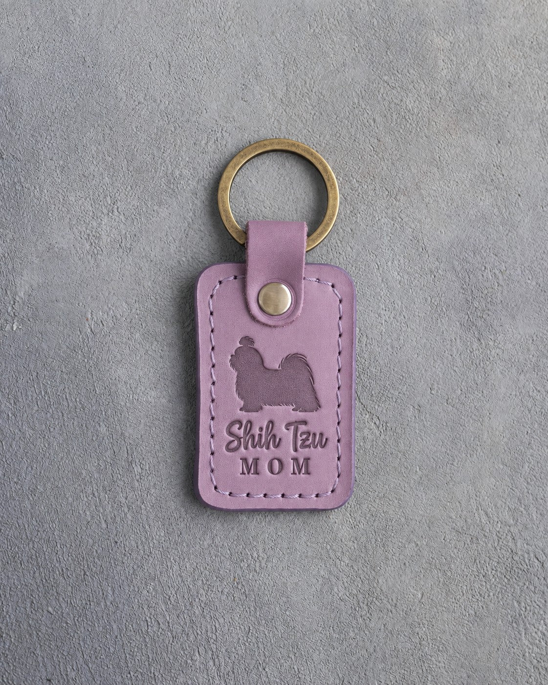Lilac leather keychain debossed with a Shih Tzu silhouette and the words Shih Tzu MOM, on gray concrete