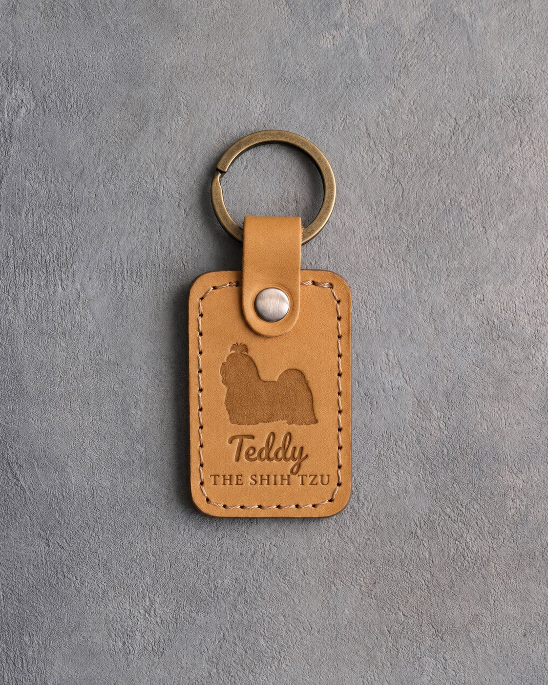 Indian Summer tan leather keychain debossed with a Shih Tzu silhouette, the name Teddy and THE SHIH TZU, on gray concrete