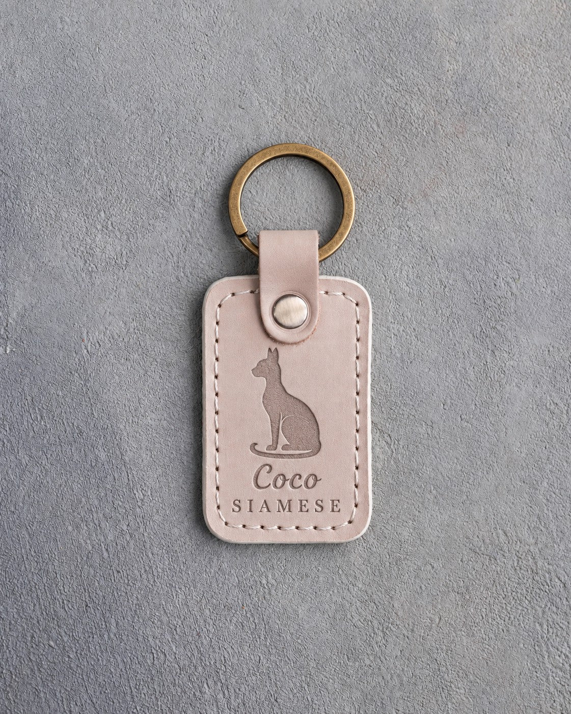 Gray sand leather keychain debossed with a sitting Siamese cat above the name Coco and SIAMESE