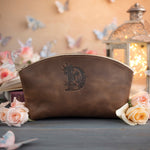 Sicilian brown initial makeup pouch with a floral monogram, staged among pale roses on a slate table