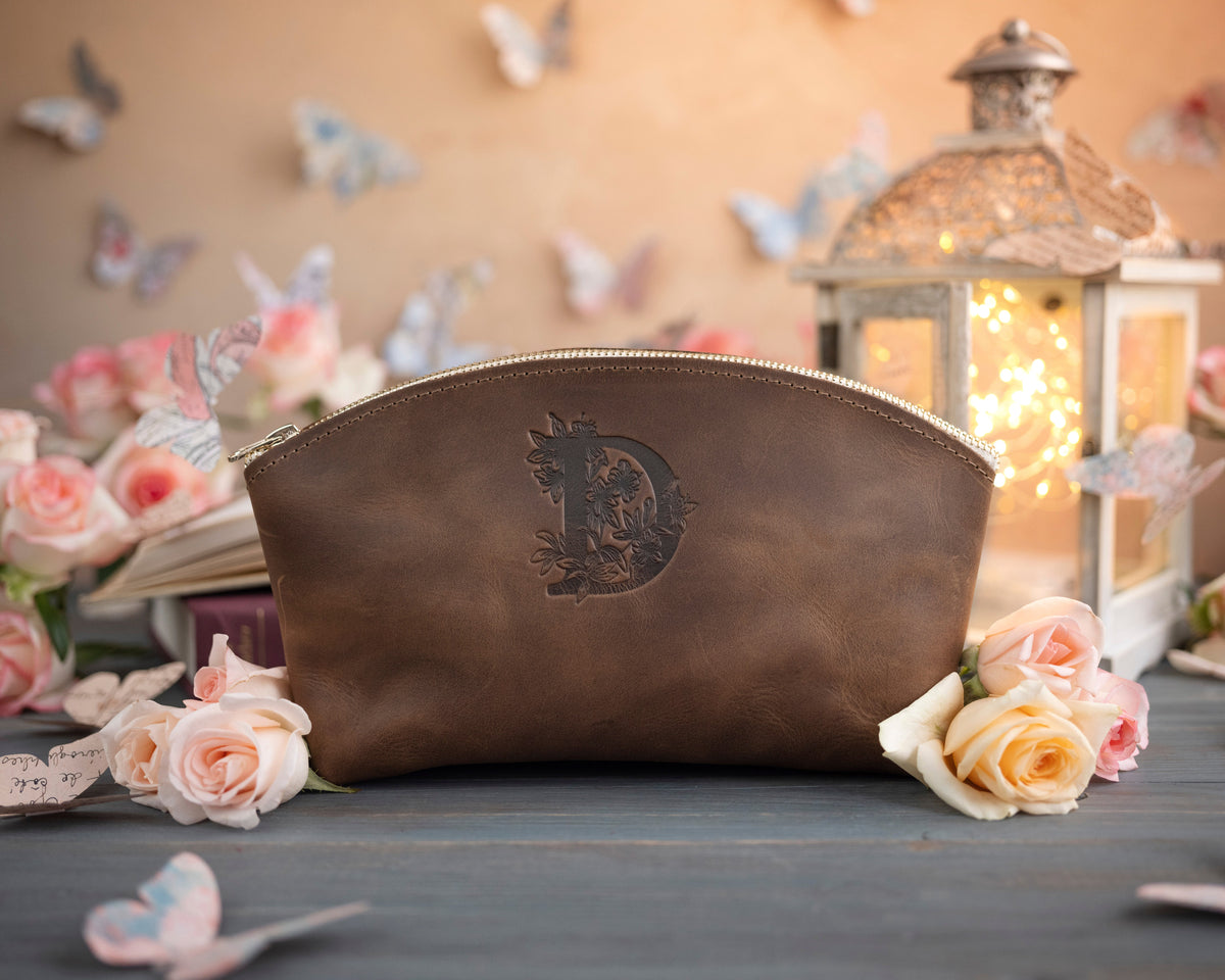 Sicilian brown initial makeup pouch with a floral monogram, staged among pale roses on a slate table