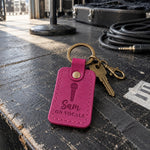 Sam ON VOCALS keychain in magenta leather clipped to a microphone bag on a stage monitor