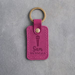 Fuchsia pink leather keychain debossed with a handheld microphone above the name Sam and ON VOCALS, on gray plaster