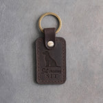 Dark espresso leather keychain debossed with a sitting mixed-breed dog and the words Sit means SIT, on gray concrete