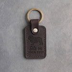 Dark espresso leather keychain debossed with an English bulldog silhouette and the words Sits on YOUR FEET, on gray concrete