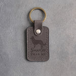 Country gray leather keychain debossed with a border collie and the phrase Smarter THAN ME, on gray concrete