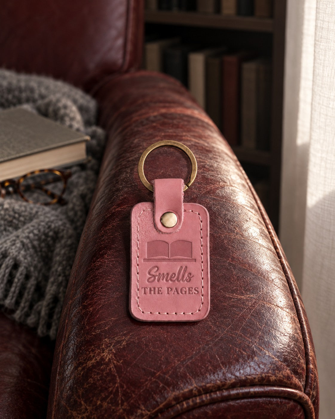 Pink Smells THE PAGES keychain resting on a fanned-open secondhand book in a sunny bookshop window