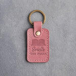 Parisian Blossom pink leather keychain debossed with an open book above Smells and THE PAGES, on gray concrete