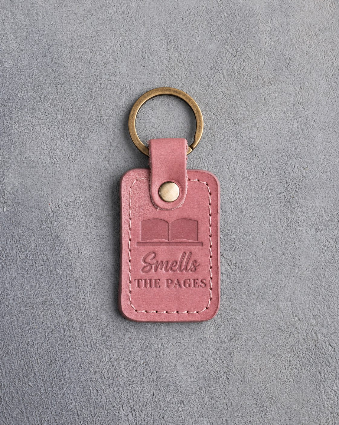 Parisian Blossom pink leather keychain debossed with an open book above Smells and THE PAGES, on gray concrete